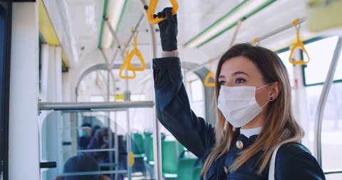 Close up portrait of beautiful blonde woman in medical mask and gloves staying at public transport. Commute bus has few passengers. Concept health and safety, coronavirus quarantine, virus protection