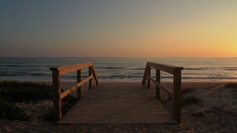 A magical golden sunset on the shores of Portugal. Wooden bridge to the beach in the foreground.