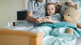 Friendly female doctor and small girl in bed in hospital, using tablet. - Powered by Shutterstock - Get 15% off with code: PIKWIZARD15