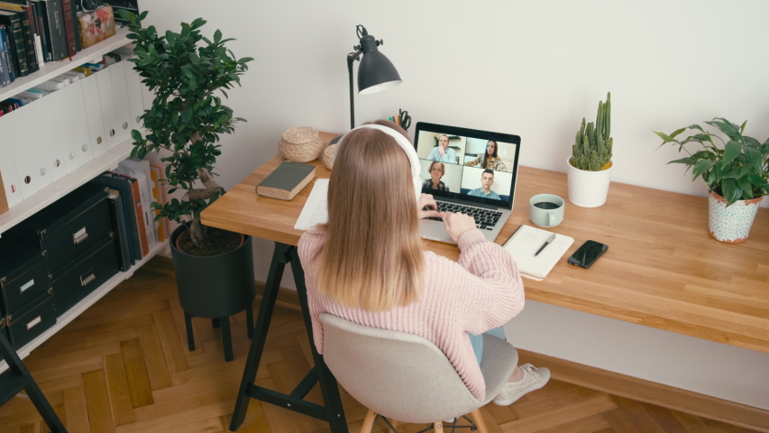 Online Group Video Call Conference of Work Team from Home Office. Woman in Headphones Greets and Talks with 4 People at Video Chat using Laptop. Self-isolation at Pandemic. 4K Top View Wide Orbit Shot Royalty-Free Stock Footage #1049553526