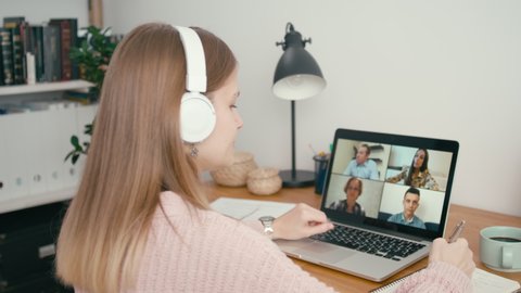 Online Group Video Call Conference of Work Team from Home Office. Woman in Headphones Talks with 4 People at Video Chat using Laptop. Self-isolation at COVID-19 Pandemic. 4K Medium Orbit Shot
