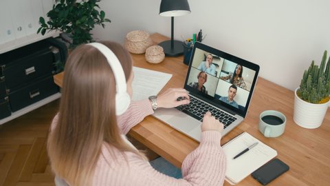Online Group Video Call Conference of Work Team from Home Office. Woman in Headphones Talks with 4 People at Video Chat using Laptop. Self-isolation at COVID-19 Pandemic. 4K Top View Medium Orbit Shot
