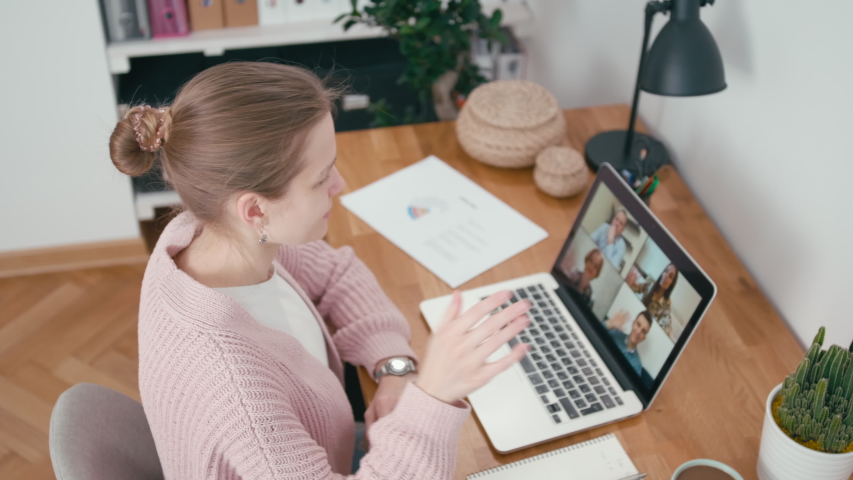 Online Group Video Call Conference of Work Team from Home Office. Woman Greets and Talks with 4 People at Video Chat using Laptop. Self-isolation at COVID-19 Pandemic. 4K Top View Orbit Shot Royalty-Free Stock Footage #1049554978