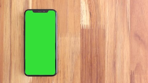 Thailand, Roi-Ed - March 30, 2020 : Smart phone place on table wood with green screen, Close-up the cell phone is on the brown desktop with chroma key, Green screen telephone, slider and top view. 