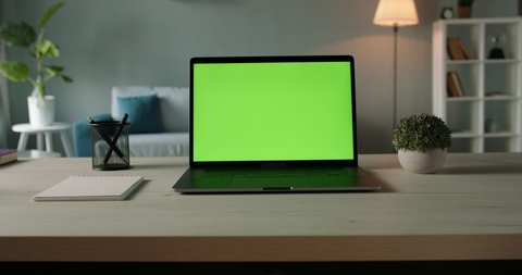 Modern laptop with mock up chroma key green screen on table of living room, desk set up for work at home - technology concept close up zoom 4k video template