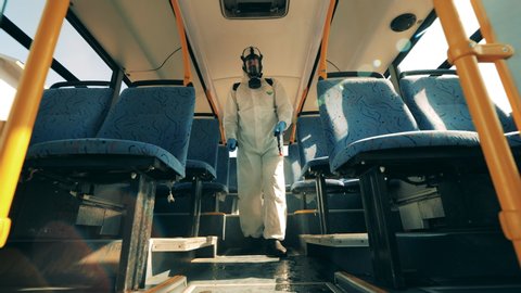Disinfector is walking along the bus and sanitizing it. Coronavirus prevention, sanitary disinfection process.