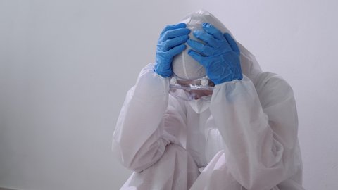 Stressed Asian doctor in PPE suit sitting on the floor, Overworked doctor