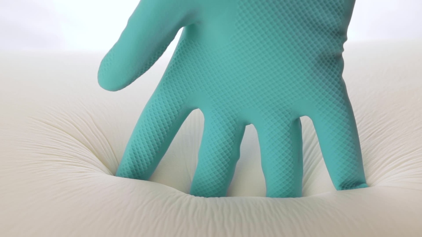 Hand with blue gloves is touching the memory foam mattress of a modern bed. Slow motion.