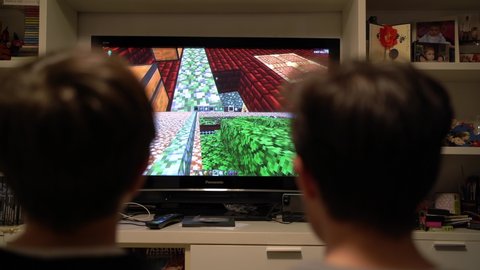 BOLOGNA, ITALY - MARCH 2020: Young brothers playing with Minecraft video games at home with play station. Minecraft is a video game created by game designer Markus Persson, better known as Notch.