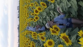 nature and children, drone view on sisters with a younger brother walk around the field with sunflowers and enjoy the fresh air in slow motion, smartphone vertical screen