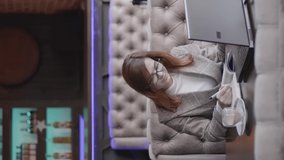 successful businesswoman in glasses drinks coffee in restaurant working on laptop computer and mobile phone, enjoys working online sitting at table by window, smartphone vertical screen