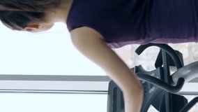 athlete girl trains muscles of legs on sports simulator in gym with large panoramic windows, smartphone vertical screen