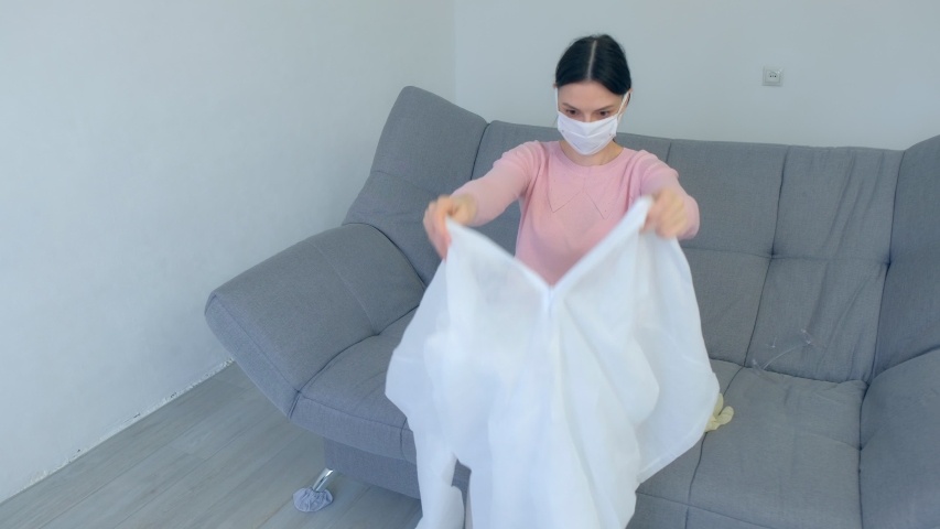 Woman is dressing on protective suit, mask, gloves and glasses. Hypochondriac at home sitting on couch, coronavirus pandemic quarantine. COVID-19 epidemic 2019-ncov. Fear of infection. Royalty-Free Stock Footage #1049581339