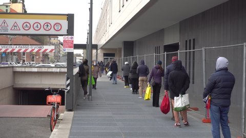 Milan, Italy, March 27, 2020: long lines at grocery stores. People stand at a distance of two meters. Desert city street during quarantine in Milan. Coronavirus COVID 19. Pandemic. Economic crisis.