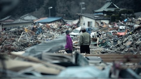 Fukushima, Japan - 03/11/2011 : a woman and a man look at the ruins of houses and organizing the search, after the tsunami