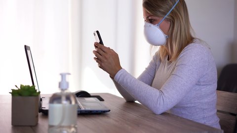 Young woman working from home wearing protective mask for Coronavirus prevention - Business girl using mobile phone in quarantine for Covid 19 - Smart work during pandemic virus crisis