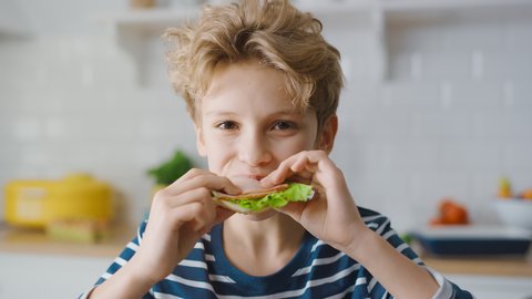 Portrait of the Cute Little Boy Eating Sandwich at the Kitchen Table. Handsome Boy Having a bite of Healthy Snack. Close-up Slow Motion Portrait