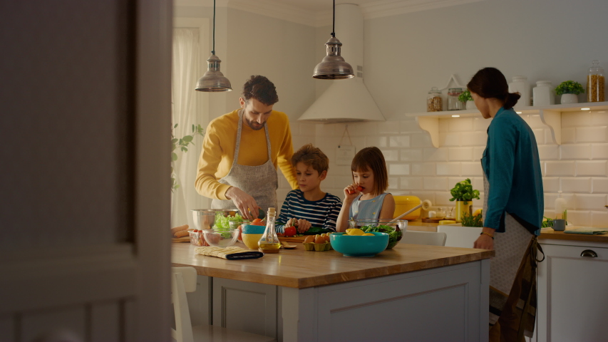 In the Kitchen: Family of Four Cooking Together Healthy Dinner. Mother, Father, Little Boy and Girl, Preparing Salads, Washing and Cutting Vegetables. Cute Children Helping their Caring Parents Royalty-Free Stock Footage #1049601256