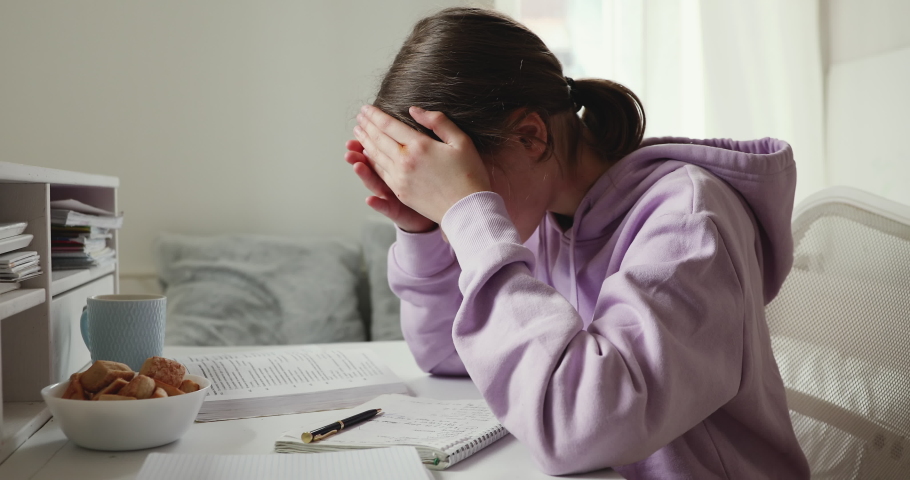 Exhausted or sick upset school student studying alone feeling headache writing difficult assignment at home. Tired depressed bored teenage girl worried about problem in children education concept. | Shutterstock HD Video #1049601526