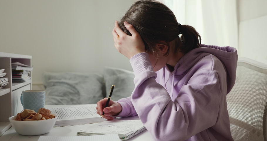 Exhausted or sick upset school student studying alone feeling headache writing difficult assignment at home. Tired depressed bored teenage girl worried about problem in children education concept. | Shutterstock HD Video #1049601526