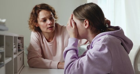 Worried young mum comforting solacing upset crying teenage daughter at home. Caring parent adult mother consoling depressed adolescent child, talking to teen girl giving love, advice, support concept.