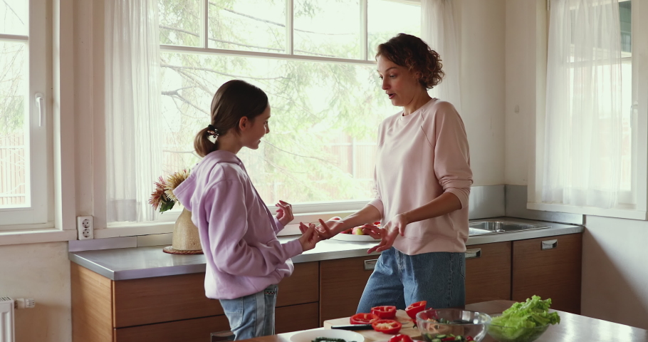 Young happy family mom and teen daughter enjoy funny dance in kitchen cooking together. Cheerful adult parent mother having fun with adolescent teenage girl preparing healthy salad at home together. Royalty-Free Stock Footage #1049601559