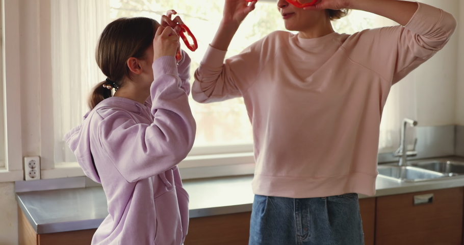 Funny young mom and teenage daughter making pepper glasses having fun. Happy teen girl helping mum in kitchen laughing, looking at camera. Cheerful vegan family enjoying cooking activity, portrait. | Shutterstock HD Video #1049601571