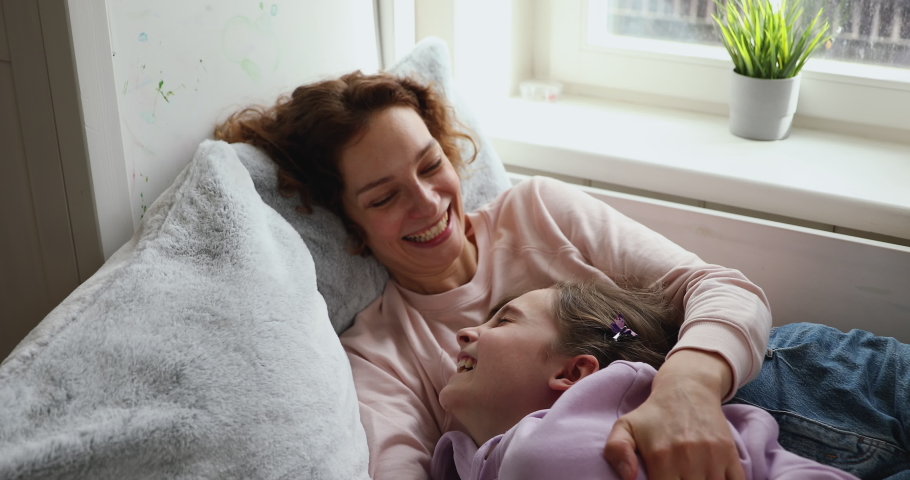 Cheerful family mother and adolescent child having fun at home. Happy young adult mum tickling funny cute teen daughter enjoying playing lifestyle game, embracing and laughing lying on bed together. | Shutterstock HD Video #1049601577
