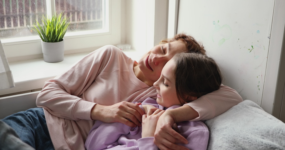 Happy loving single mom hugs cute teenage child daughter talking and relaxing lying in bed at cozy home. Young mother embracing teen girl enjoying sweet moments of parent and kid bonding together. Royalty-Free Stock Footage #1049601580