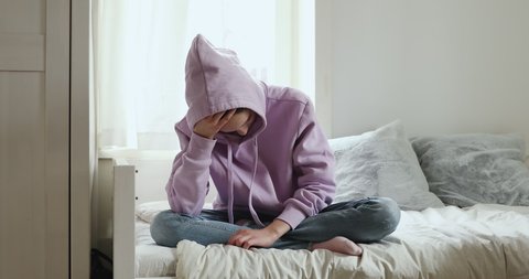Unhappy depressed teenager girl wears hood sits alone on bed thinking of problem. Sad sensitive lonely adolescent teen feeling worried and hurt at home. Teenage psychological trauma, complex concept.