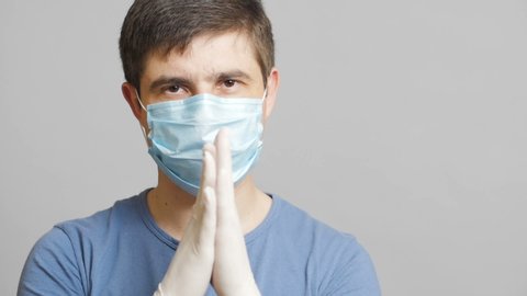 man with humor in surgical mask and sterile gloves on a gray background rubbing his hands slyly, concept medicine joke,strange doctor