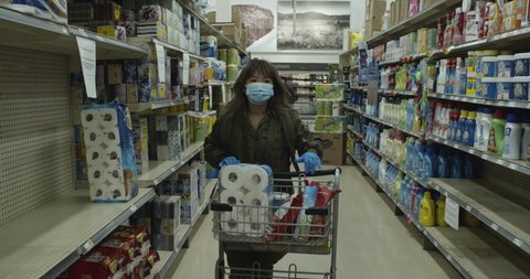 MONTREAL, QUEBEC - MARCH 27, 2020: Shopper walks in grocery style aisle picking up toilet paper from an almost empty shelf during the coronavirus pandemic