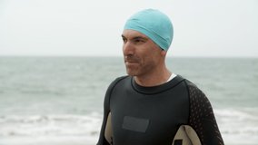 Sportsman wearing goggles on beach. Male swimmer wearing sportswear and protective glasses near body of water at cloudy day, handheld shot. Triathlon concept