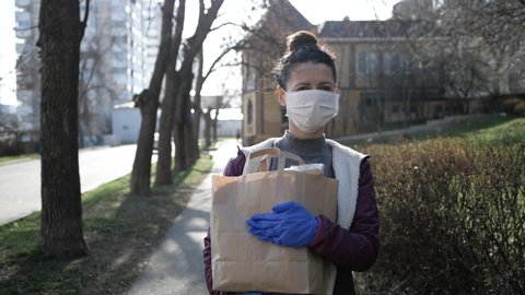 food delivery young woman in protective mask and gloves carries bag with products from store. pandemic.
