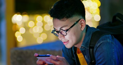 asian young man win mobile games on smart phone with fist gesture outdoor in the city at night