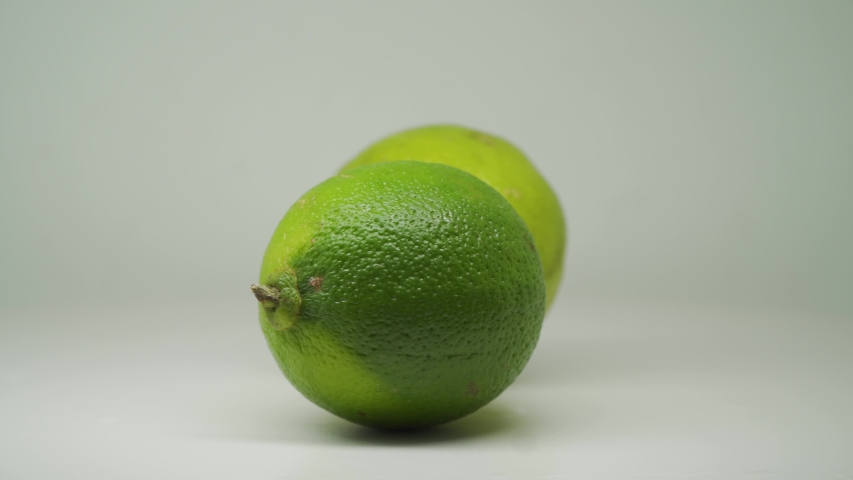 Two Green Limes On Top Of The White Background Table Turning Clockwise - Close Up Shot