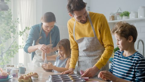 In the Kitchen: Family of Four Cooking Muffins Together. Mother and Daughter Mixing Flour and Water to Create Dough for Cupcakes, Father, Son Preparing Paper Lines for Pans. Children Helping Parents