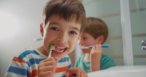 Adorable kid brushing his little white teeth in the bathroom looking directly into camera. Portrait shot.