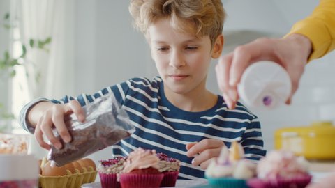 In the Kitchen: Portrait of the Smart Little Boy Sprinkling Funfetti on Creamy Cupcakes Frosting. Family Cooking Muffins Together. Adorable Children Helping their Caring Parents