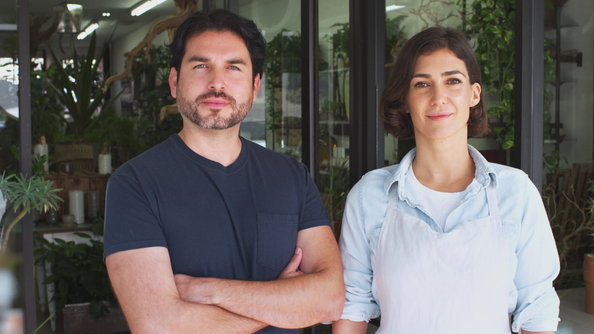 Male and female owners of florists shop standing in doorway of store looking into camera and smiling - shot in slow motion