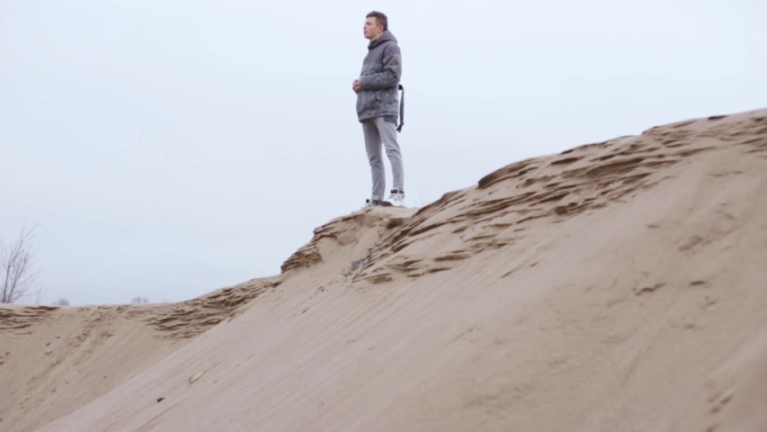 Young man is standing on sand dune. Pacified male traveler enjoying cloudy landscape while traveling in desert
