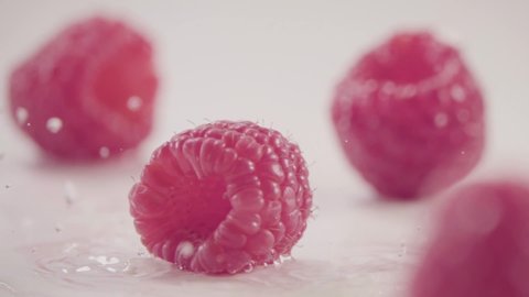 Raspberry falls down on heap of fresh berries with water drops slow motion