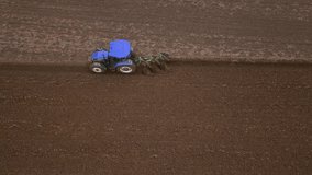 Top view side view of a blue tractor plowing a field, ground furrow
