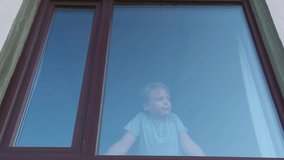 Closeup view video portrait of cute angry mad young white boy unhappy to have staying home. Kid watching sadly out of window through glass.