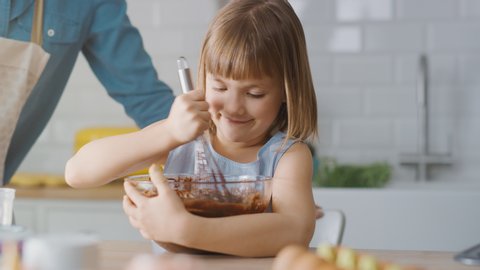 In the Kitchen: Portrait of the Cute Little Daughter Mixing Flour and Water to Create Dough for Cupcakes. Family Cooking Muffins Together. Adorable Children Helping their Caring Parents