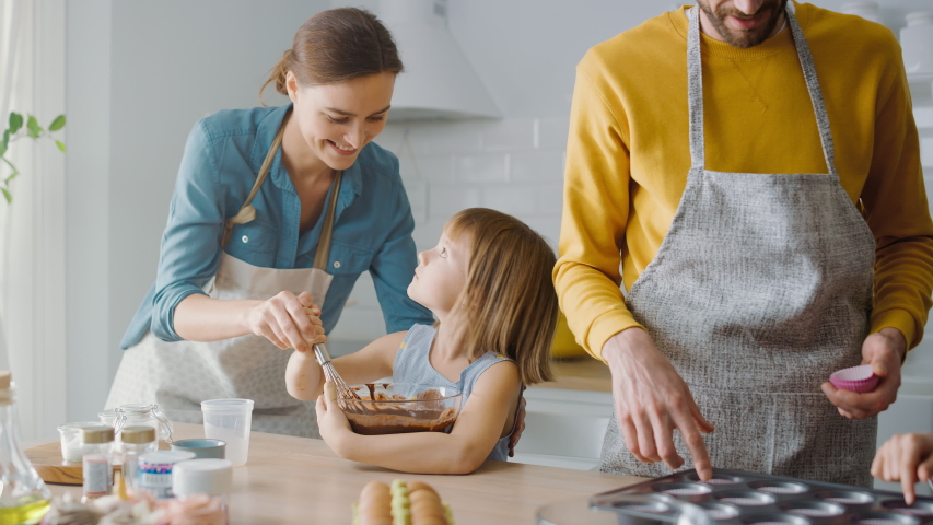 In the Kitchen: Family of Four Cooking Muffins Together. Mother and Daughter Mixing Flour and Water to Create Dough for Cupcakes, Father, Son Preparing Paper Lines for Pans. Children Helping Parents Royalty-Free Stock Footage #1049665552