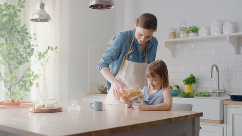 Breakfast in the Kitchen: Young Beautiful Mother Pours Cereal into Bowl, Adorable Little Daughter Starts Eating with Pleasure. Caring Mother Prepares Cereal Breakfast for Her Cute Little Girl