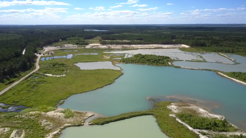 amazing panorama of wide tranquil lake with green islands and spits against sand quarry in summer aerial view. Concept environmental change