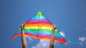 Closeup view video of two kids hands holding bright colorful kite overhead isolated at bright clear blue sky background.