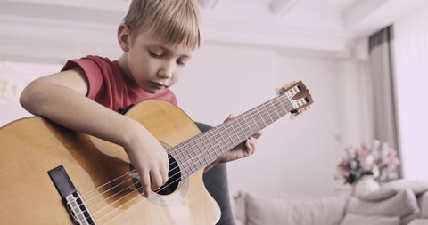 Young boy with a guitar. Boy of 8 years plays the classical guitar. The caucasian child learns to play the guitar. 
Real time. Zoom in. Natural lighting. Low angle view.